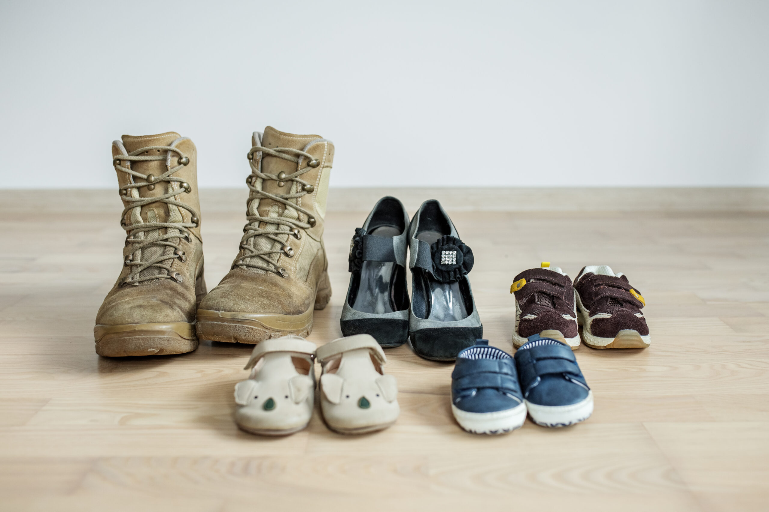 old worn military boots, women's shoes and lot of baby shoes on wooden floor. Military father and family concept. Copy space