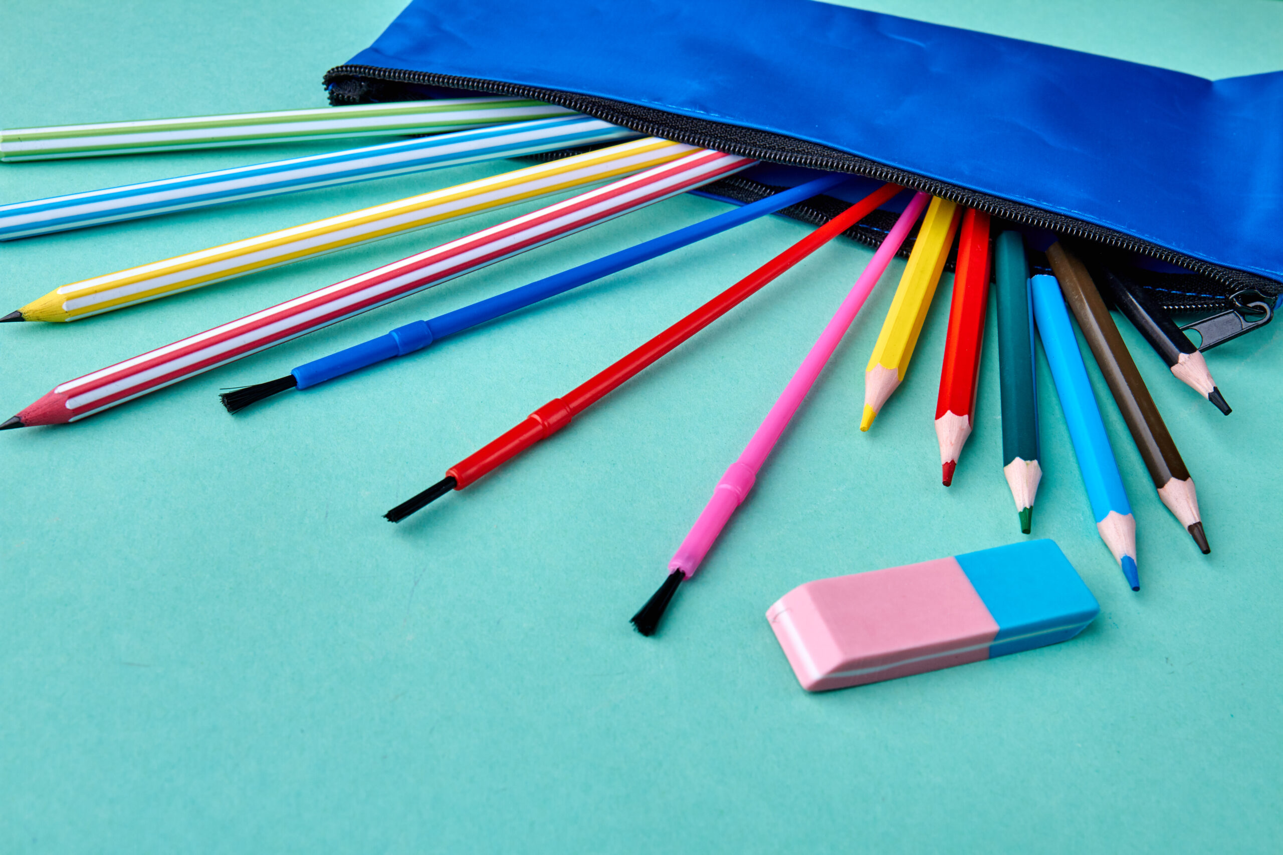 Set of colored pencils scattered on color background. Case with pencils and eraser on turquoise background.